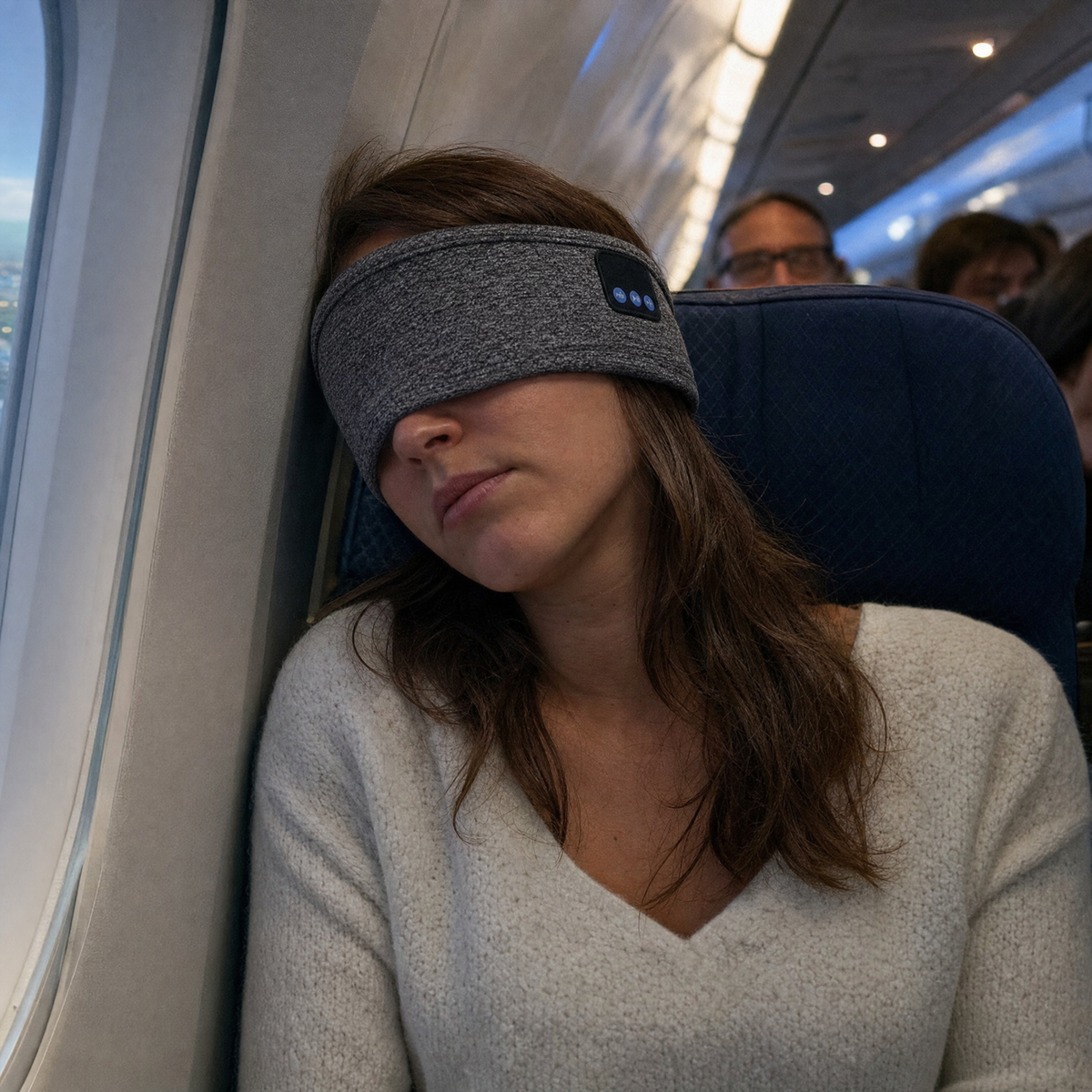 Woman asleep in an aeroplane window seat with the VESU Sleep Headband pulled down over her eyes as a sleep mask